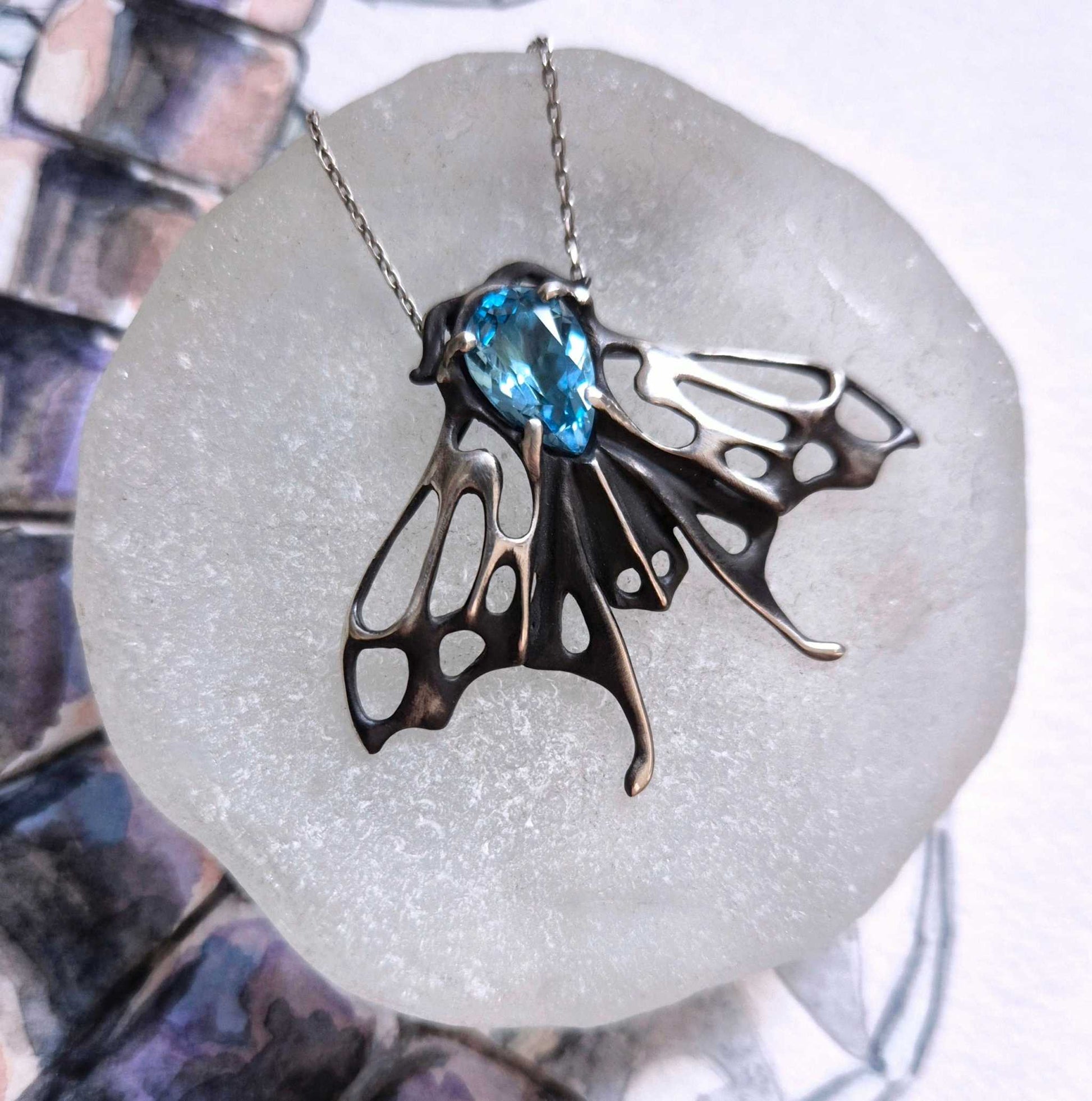 Overhead view of the silver Moth necklace on a ceramic surface, showing gemstone sparkle and sculpted wings.