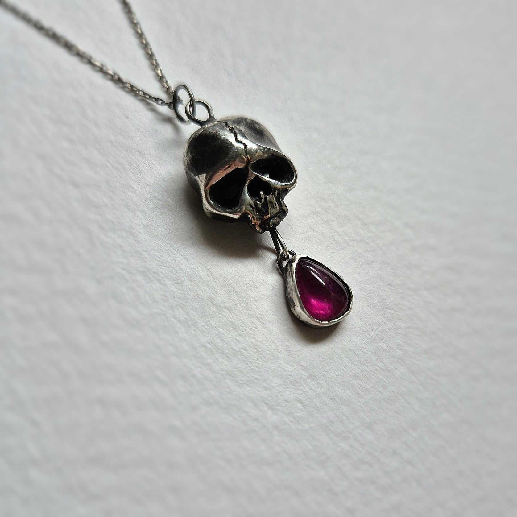 Close-up of handmade oxidized silver Skull necklace with a rhodolite garnet on matte surface