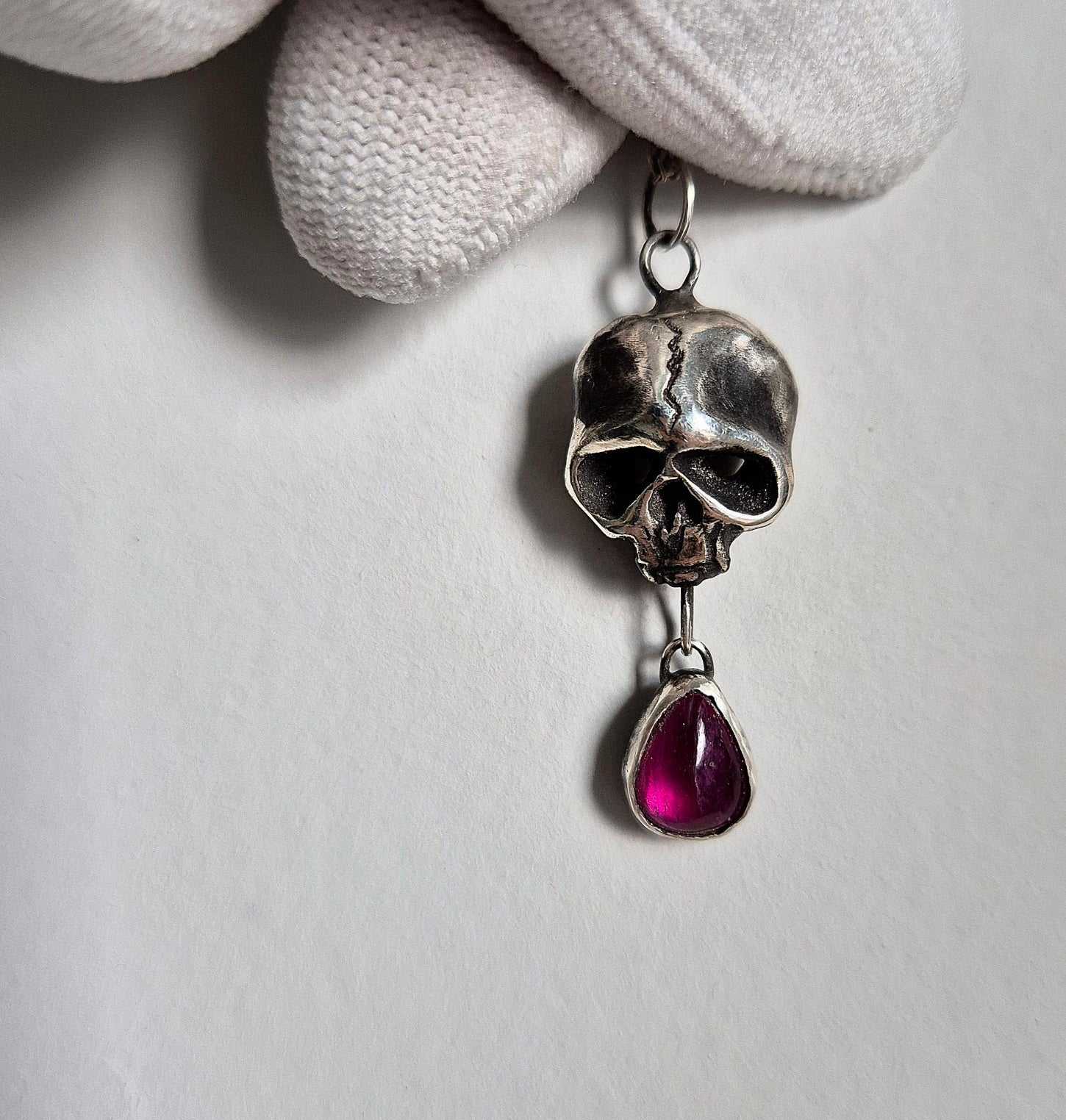 Macro shot of handmade oxidized silver Skull necklace, set with roughly polished garnet