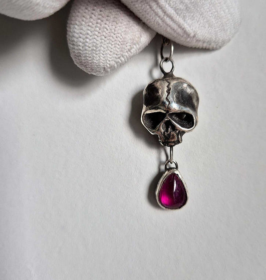 Macro shot of handmade oxidized silver Skull necklace, set with roughly polished garnet