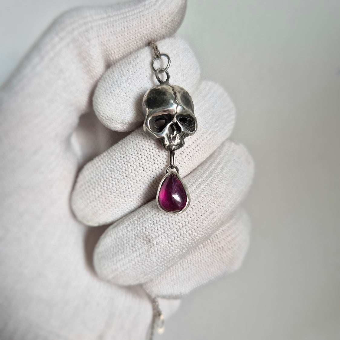 Close-up of oxidized silver Skull necklace with a roughly polished red gem