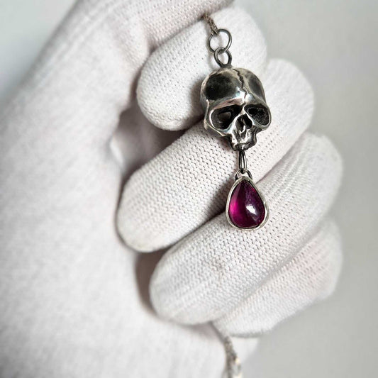 Detailed view Silver Skull necklace with red garnet charm, photographed  in hands