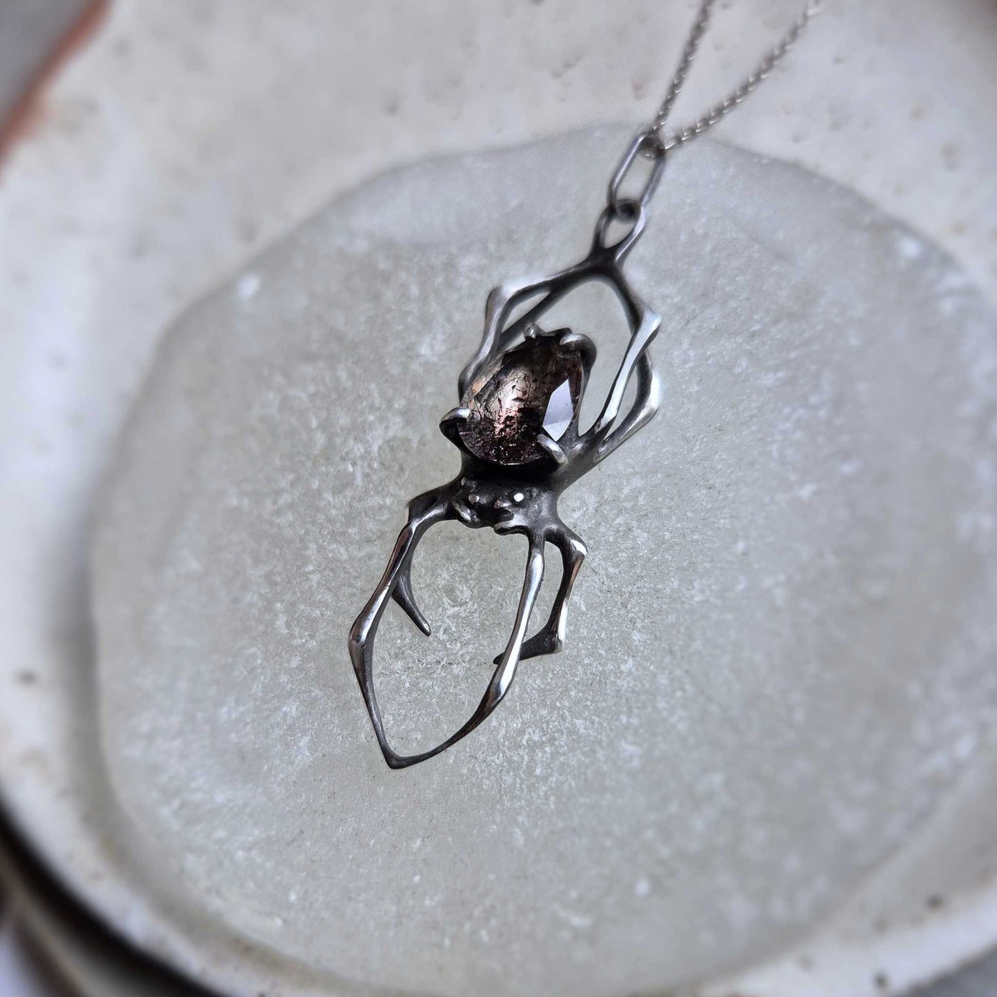 Detailed view of silver Spider pendant with Super Seven crystal on minimalist surface