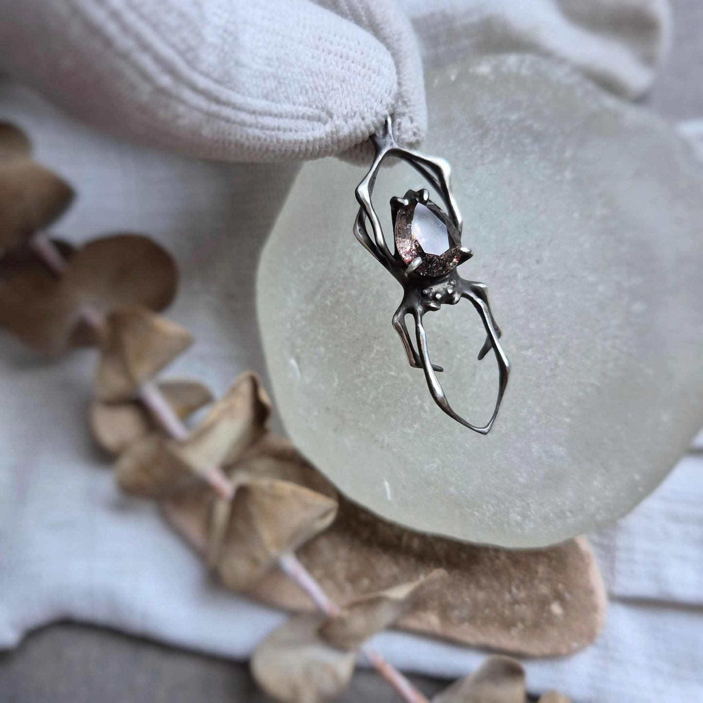 Silver Spider necklace in gloved fingers styled on pale background with visible gemstone texture