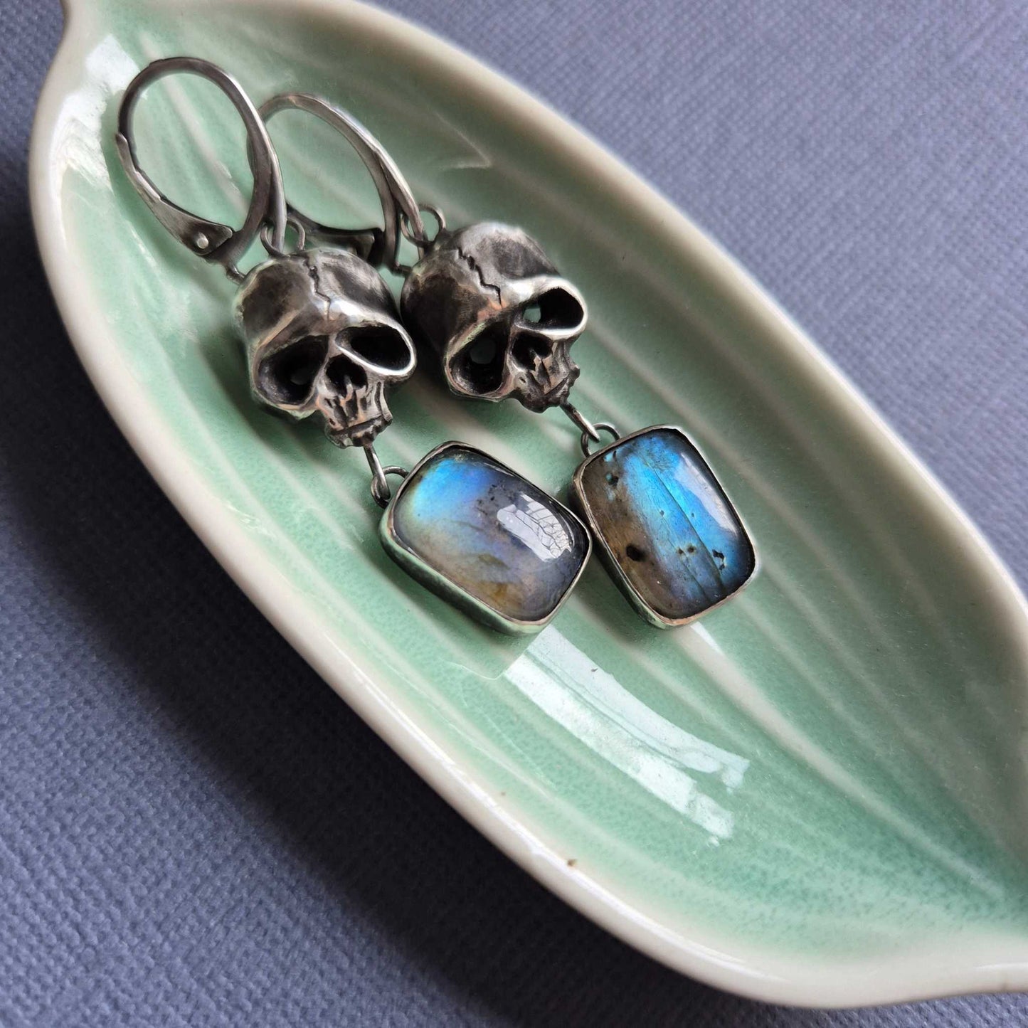 Close-up of handmade oxidized silver Skull earrings with blue labradorite gemstones in soft lighting