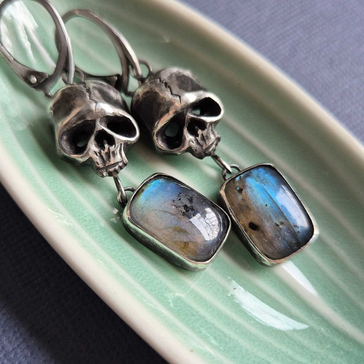 Close-up of handmade oxidized silver Skull earrings with blue labradorite gemstones in ceramic trinket