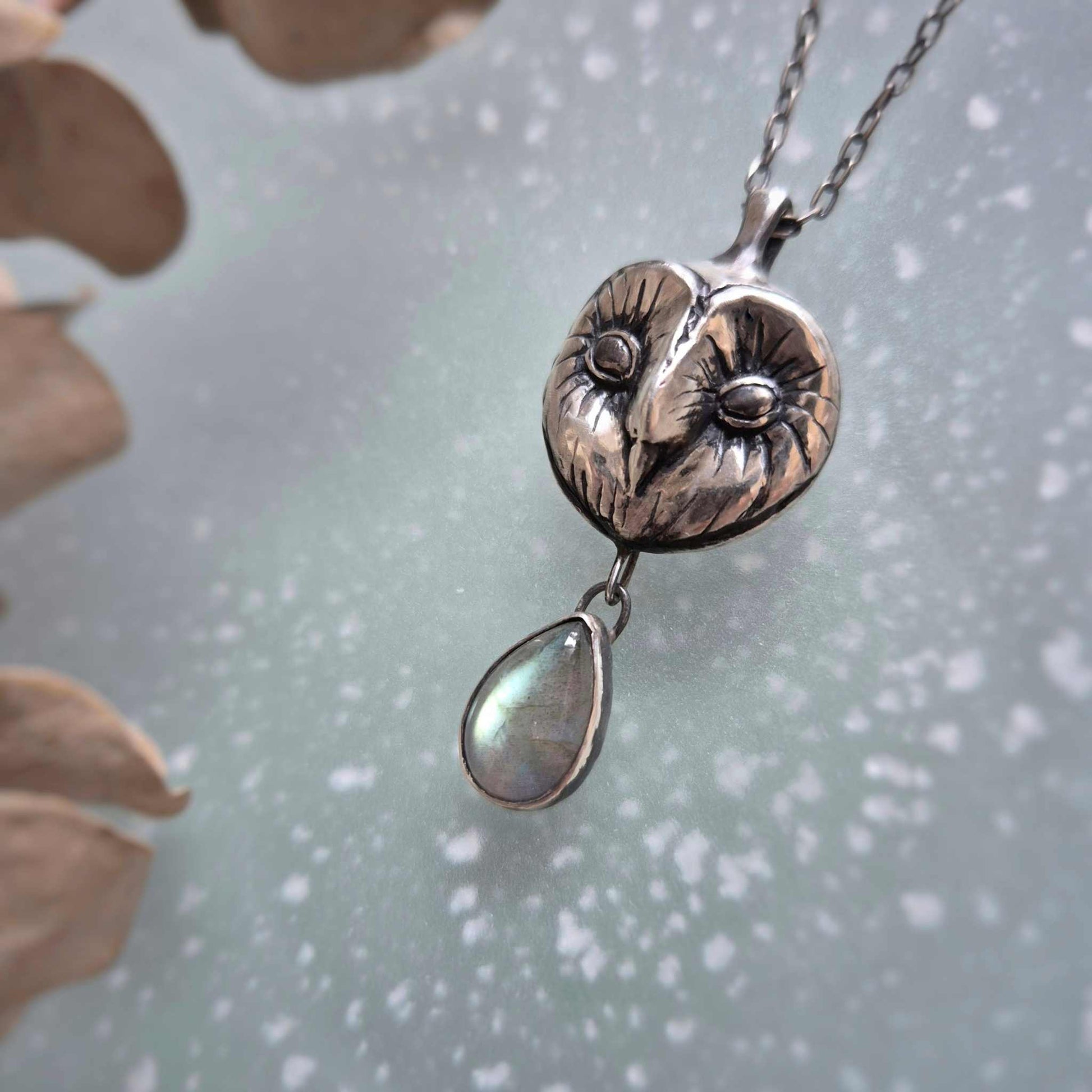 Nature-inspired silver Owl necklace with Barn owl face and labradorite drop, handmade and tactile, on matte glass surface