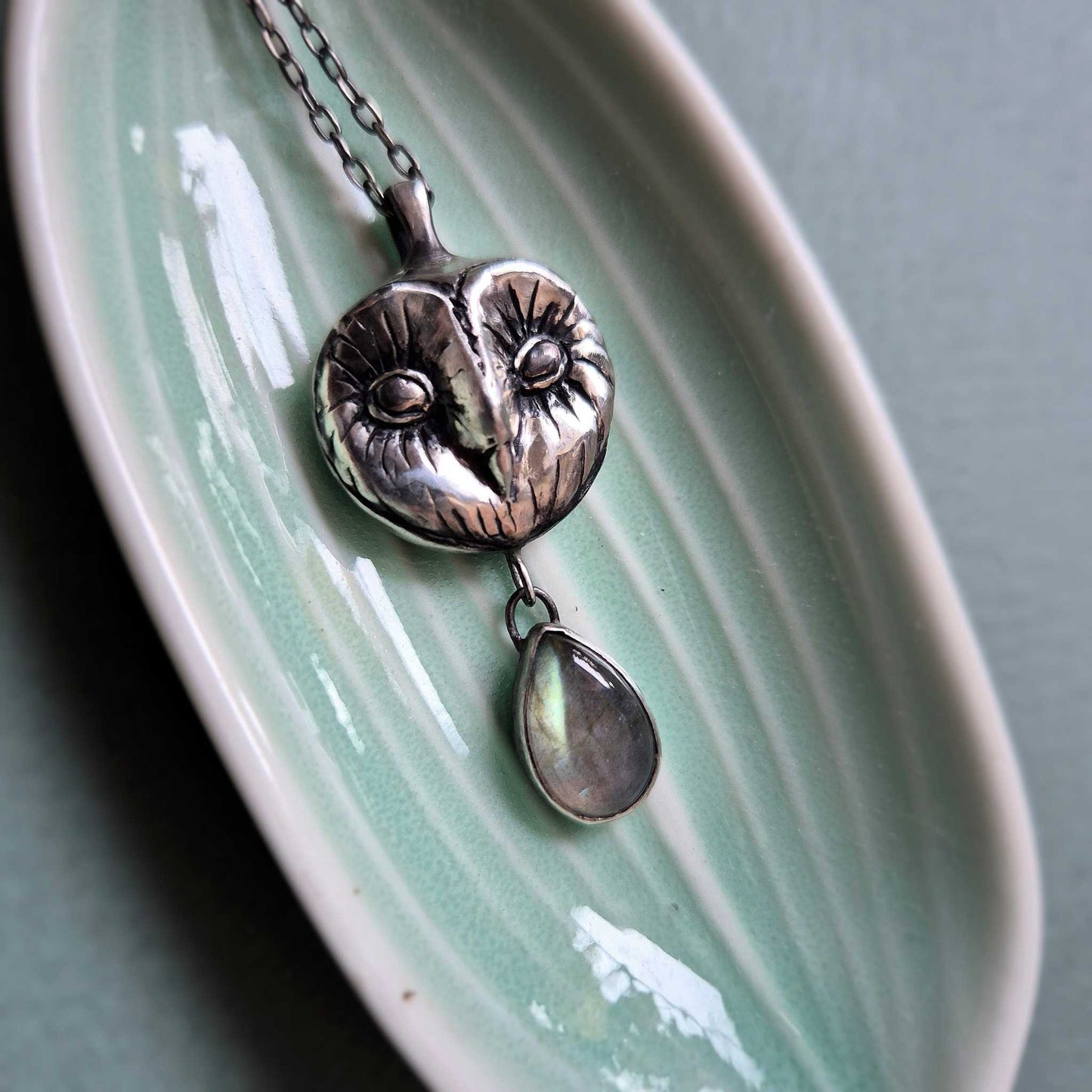 Close-up of a handcrafted silver Owl necklace featuring a stylized Barn owl face and a teardrop labradorite drop.