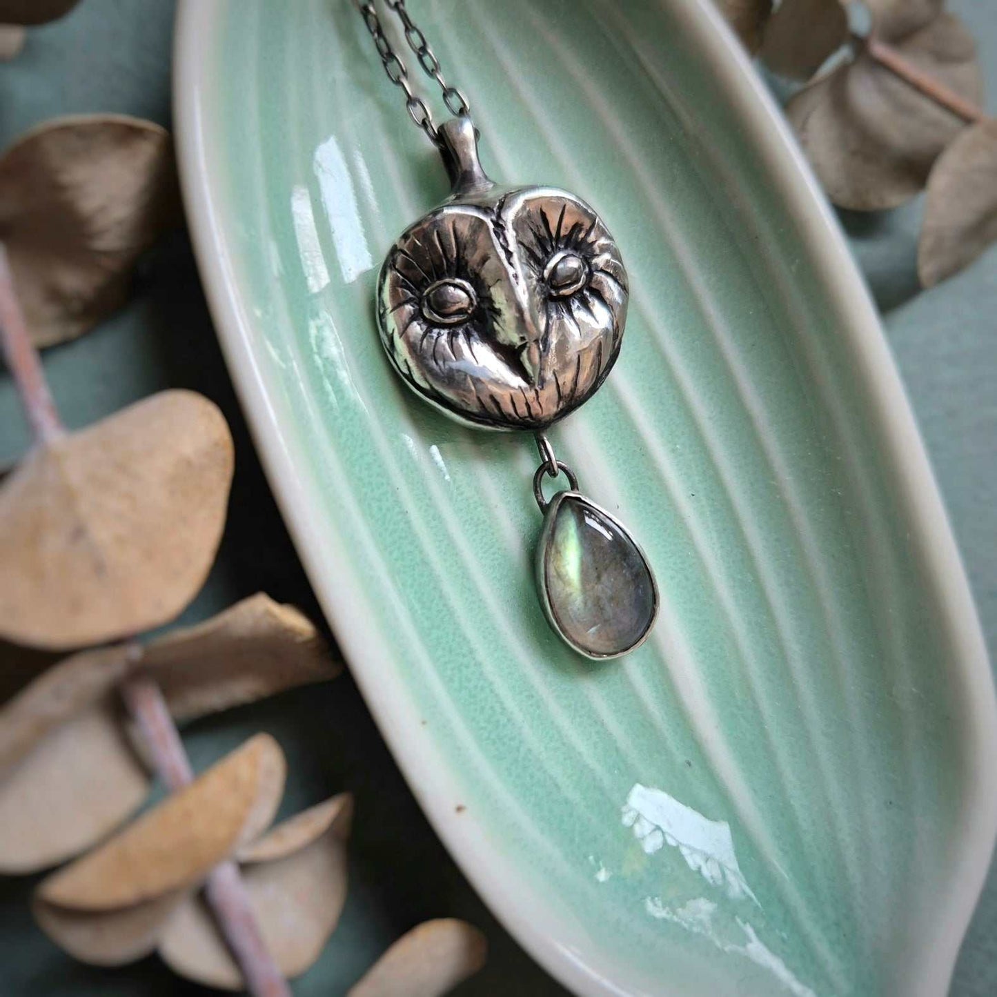 Flatlay of silver Owl necklace styled on a leaf-shaped ceramic plate, evoking forest tones.
