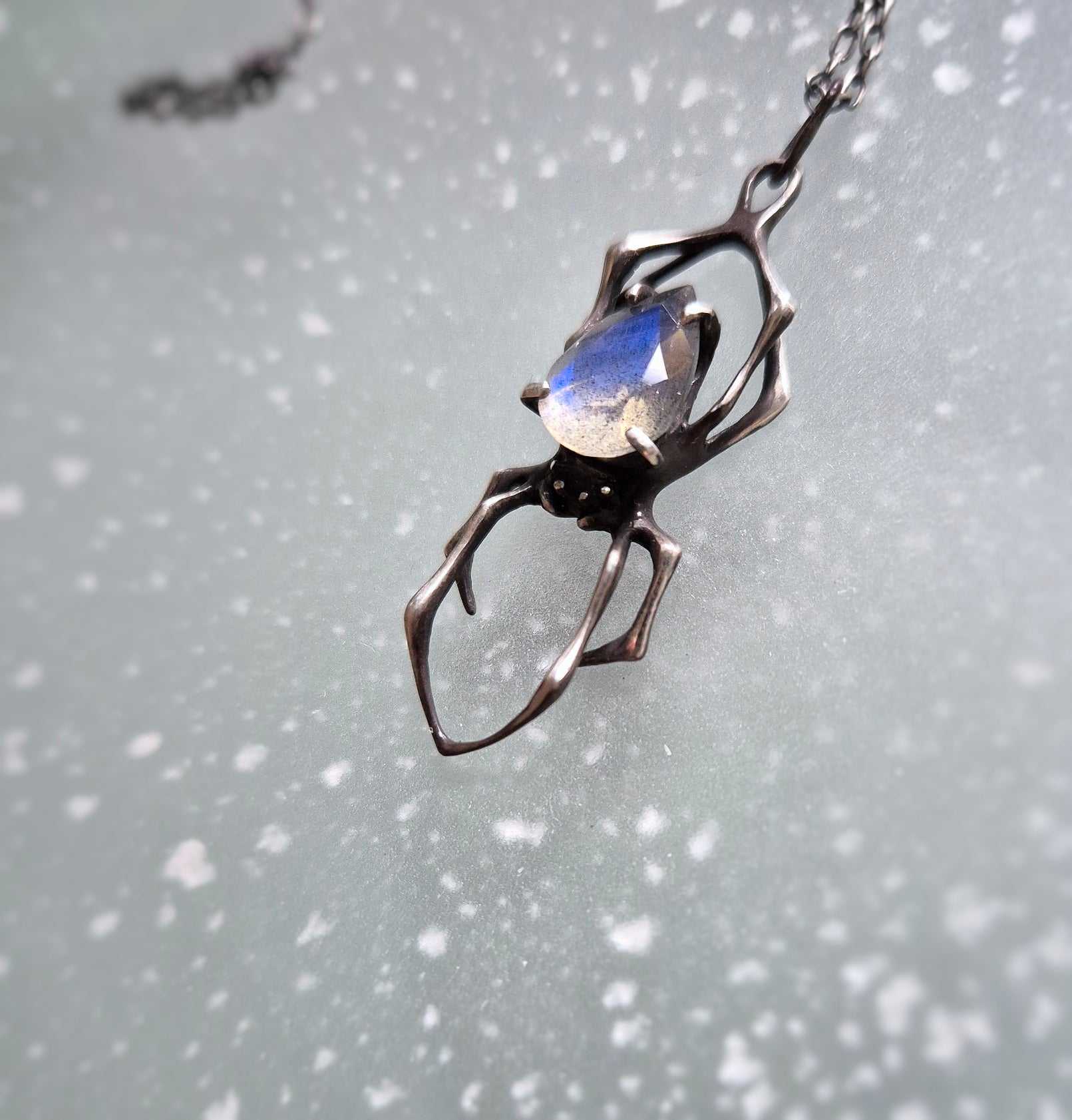 Silver spider pendant with labradorite, photographed on textured background