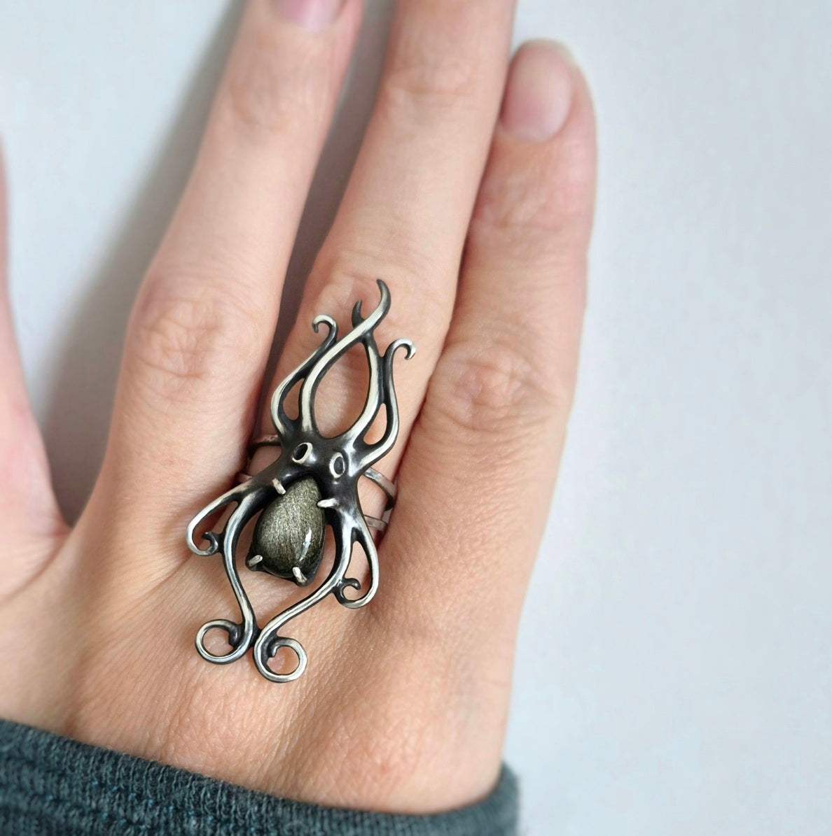 Close-up of handmade octopus-shaped silver ring on finger, with elegant curved tentacles