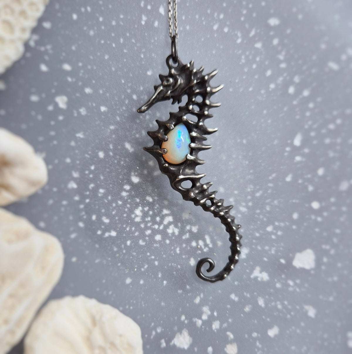 Silver Seahorse necklace with sculpted texture and natural opal on textured gray background