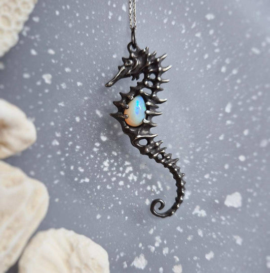 Silver Seahorse necklace with sculpted texture and natural opal on textured gray background