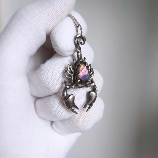 Oxidized silver Scorpion pendant with a vivid labradorite flash, held in a white glove.