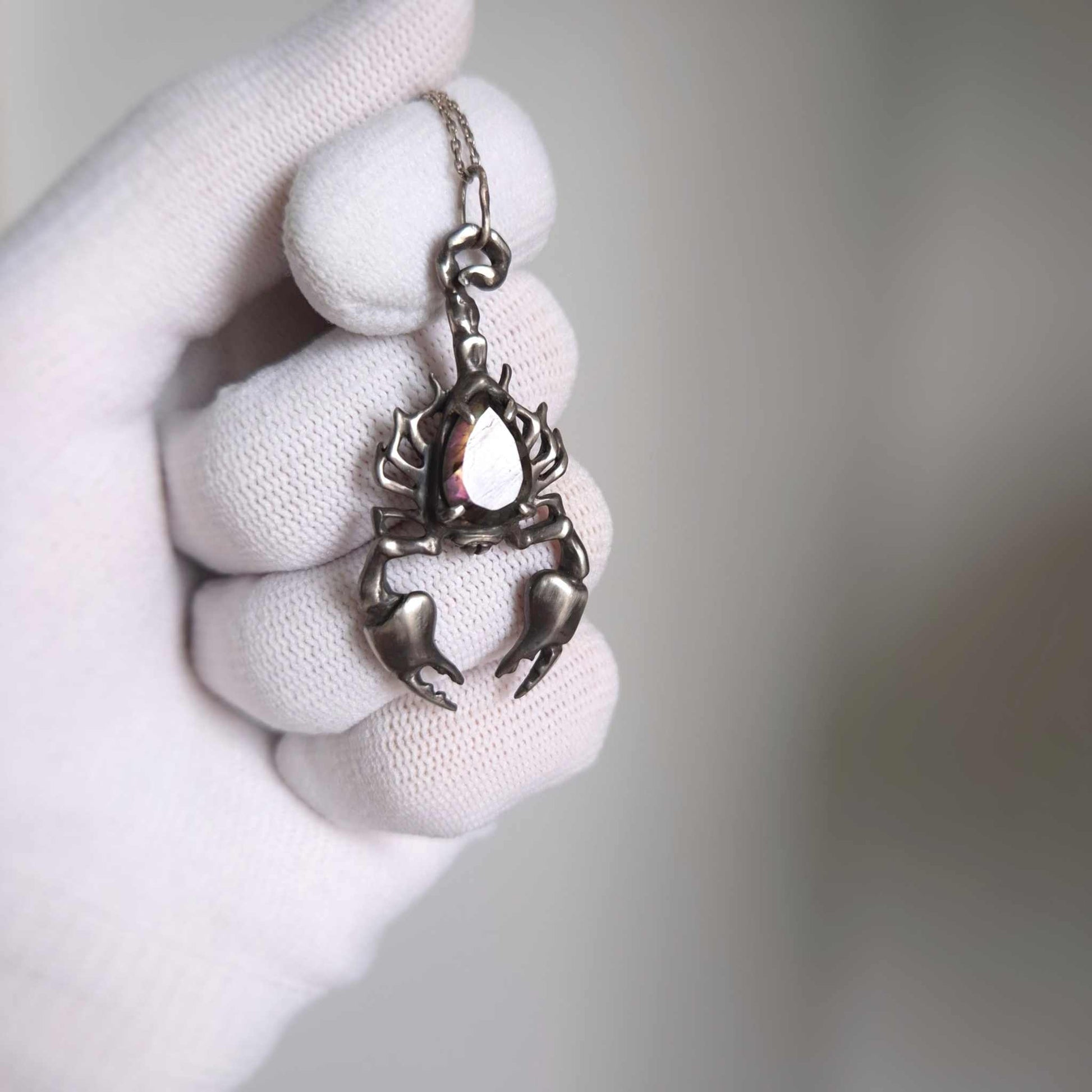 Close-up of a faceted labradorite in a Scorpion setting, glowing with soft iridescence, in gloved hand