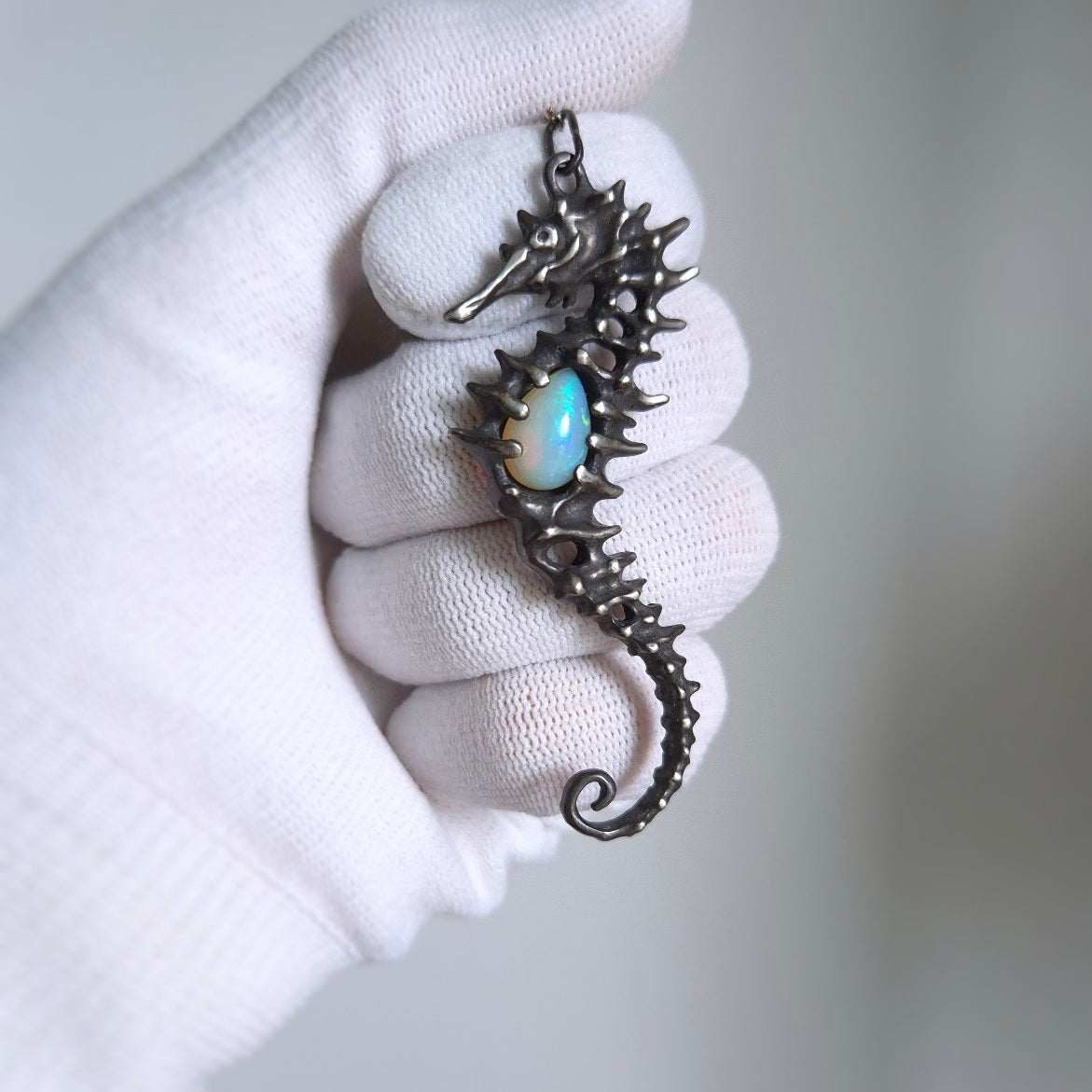 Silver Seahorse necklace featuring a opal gemstone, displayed in a gloved hand