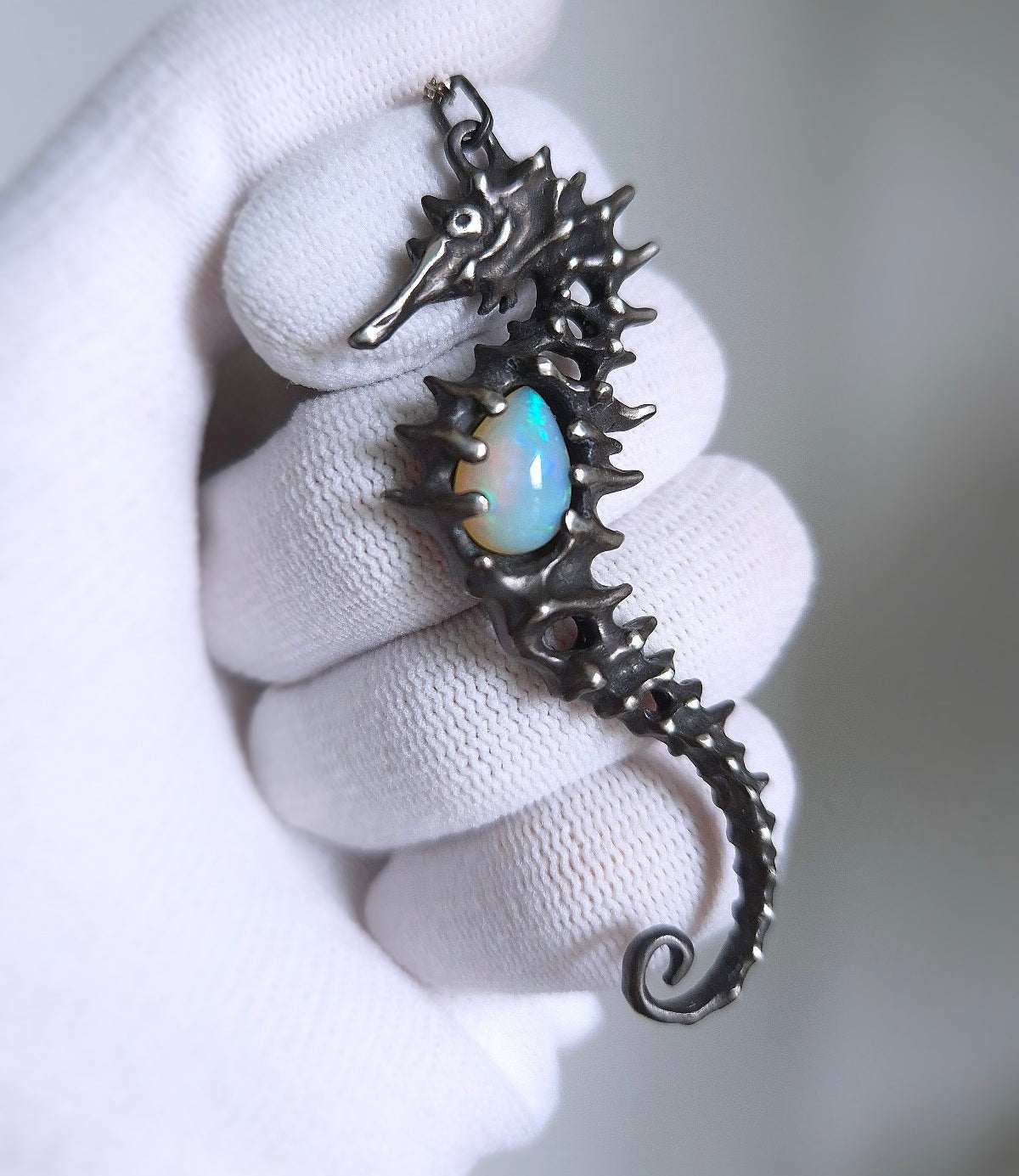 Handmade Silver Seahorse necklace featuring a natural opal gem, displayed in a gloved hand