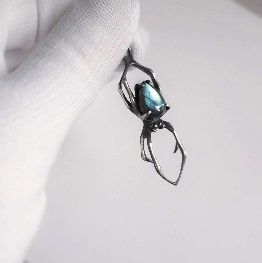 Close-up silver spider necklace with labradorite, held between fingers