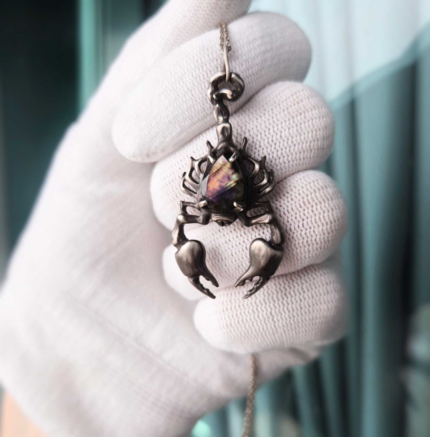 Handcrafted silver Scorpion necklace with multicolor labradorite, shown in a white-gloved hand.