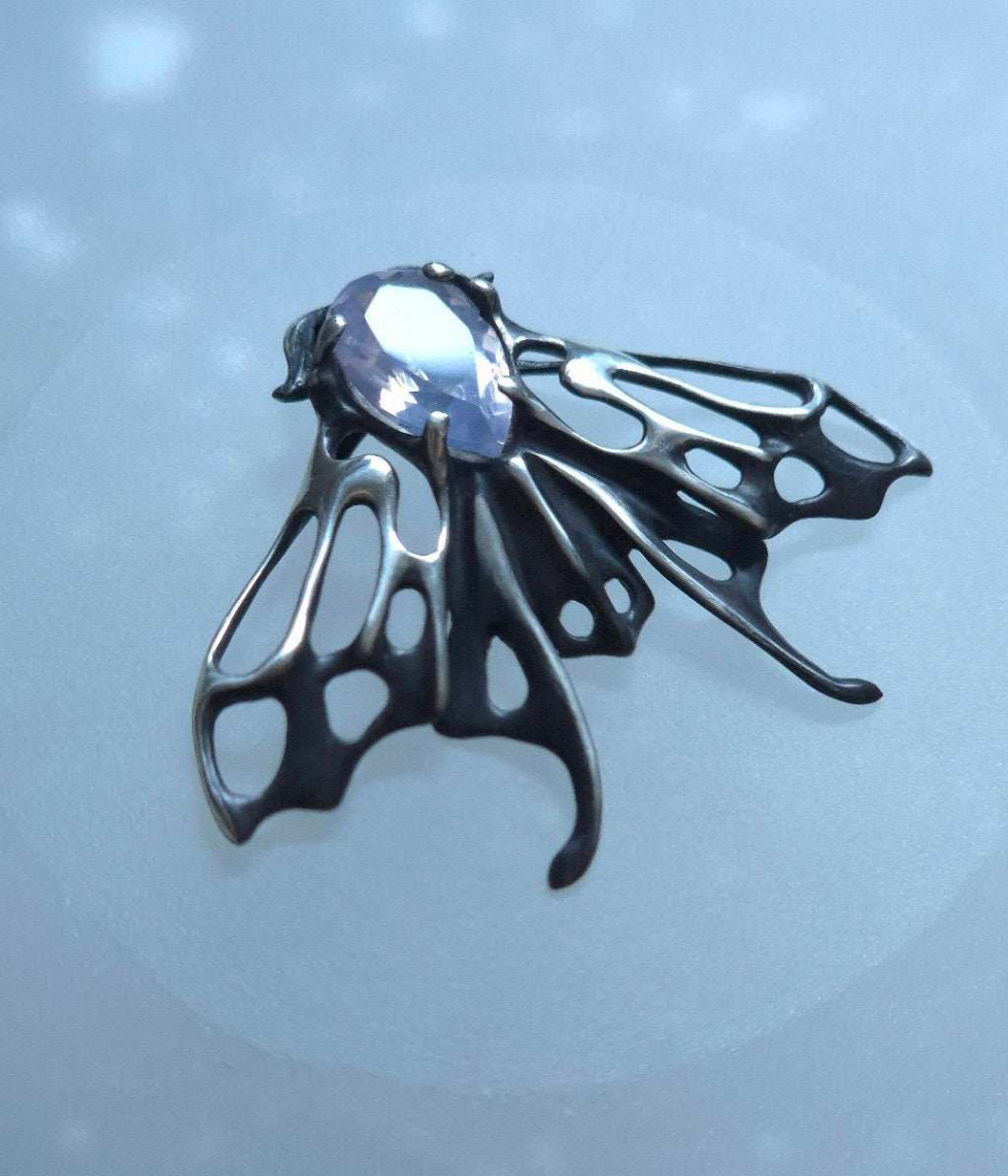 Detailed view of sculptural silver Moth necklace featuring a translucent lavender gem