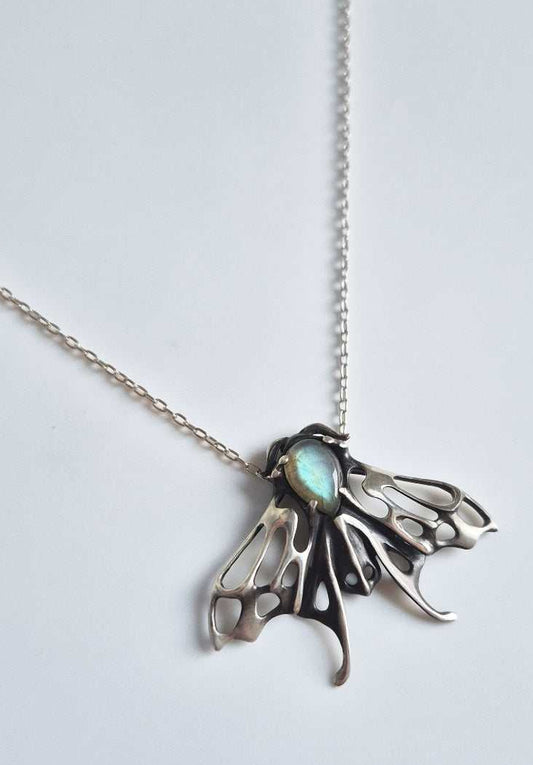 Angled silver moth pendant with cyan-flash labradorite and chain against white