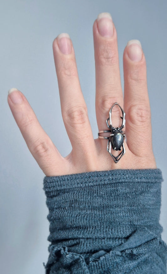 Sterling silver spider ring worn on a hand, showing its adjustable double band and scale