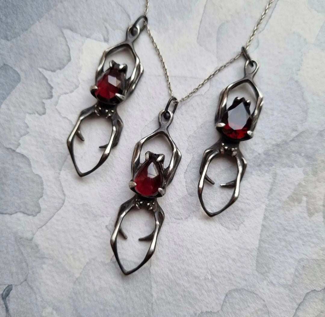 Silver spider necklaces photographed on textured background – garnet gemstone jewelry detail