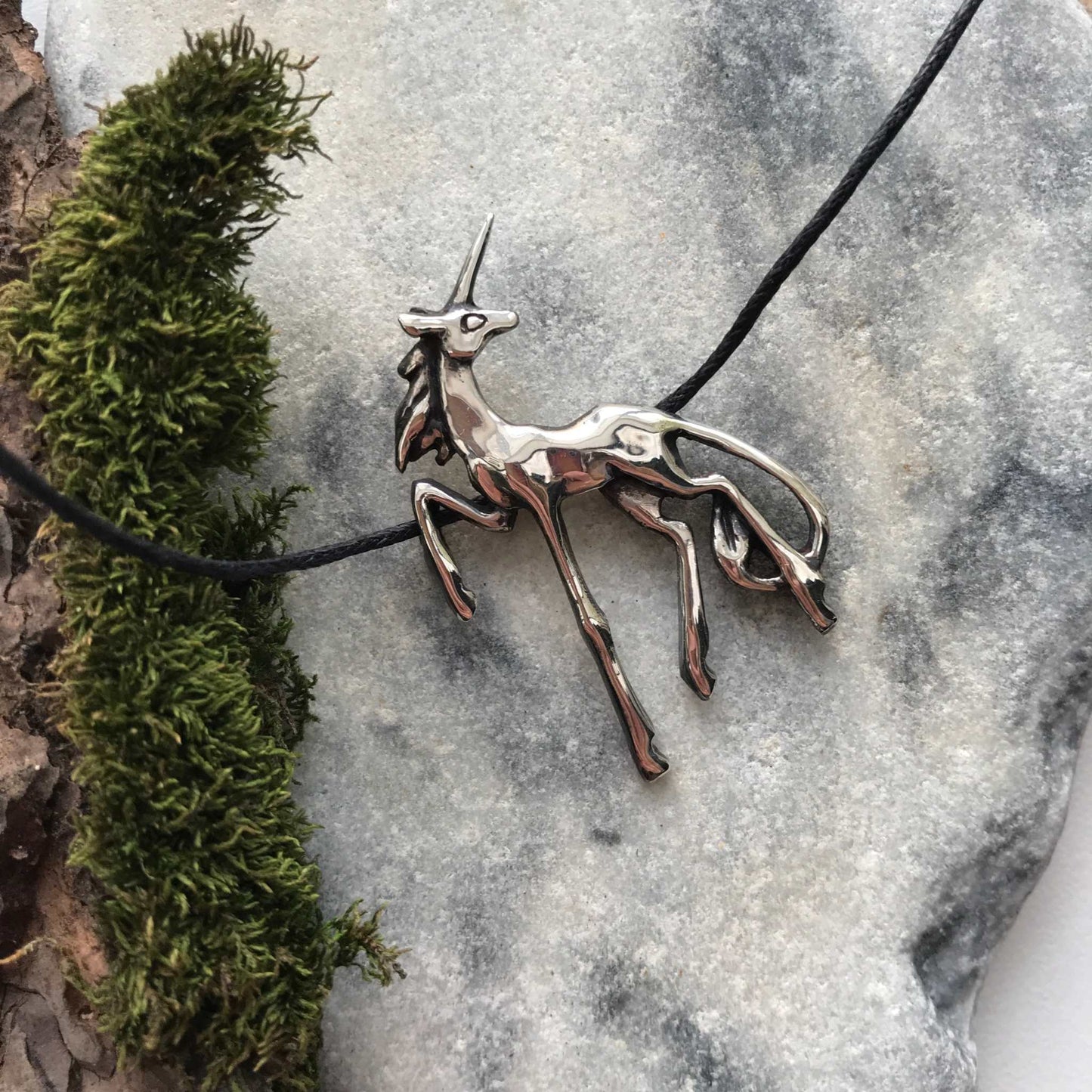 Artistic silver Unicorn necklace styled with natural textures and moss, reflecting mythical woodland vibes.
