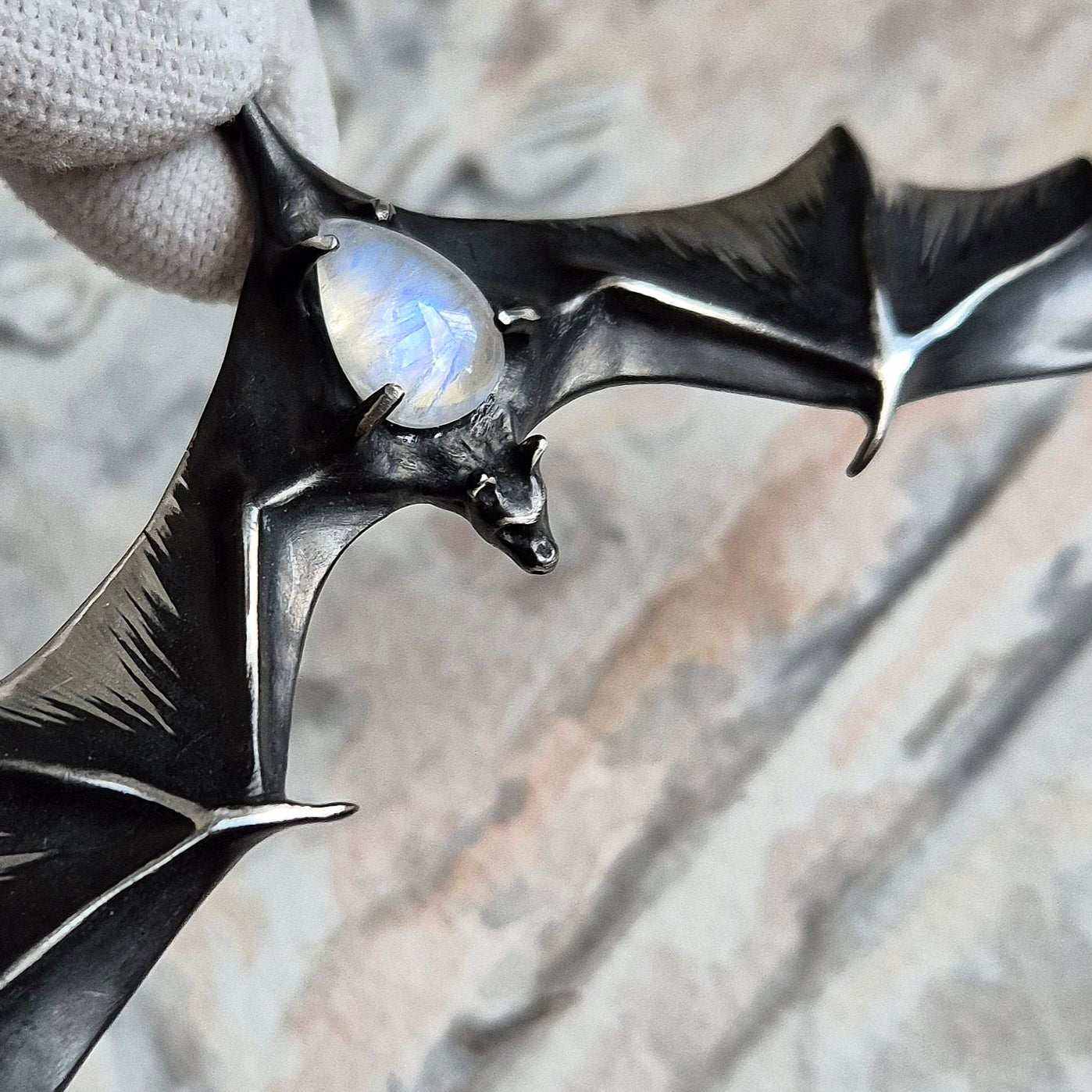 Close-up of silver Bat necklace with moonstone gem, showing sculpted wing shape.