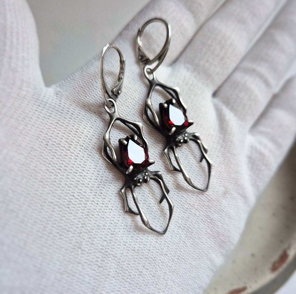 Detailed view Silver Spider earrings with Mozambique red garnets in hands