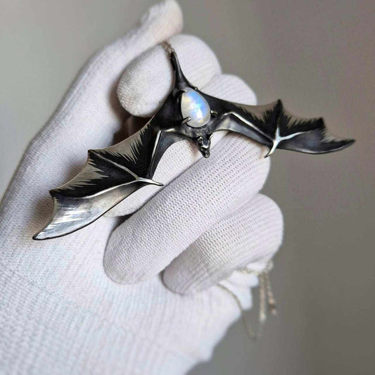Silver Bat necklace with rainbow moonstone, held in gloved hand for scale and detail.
