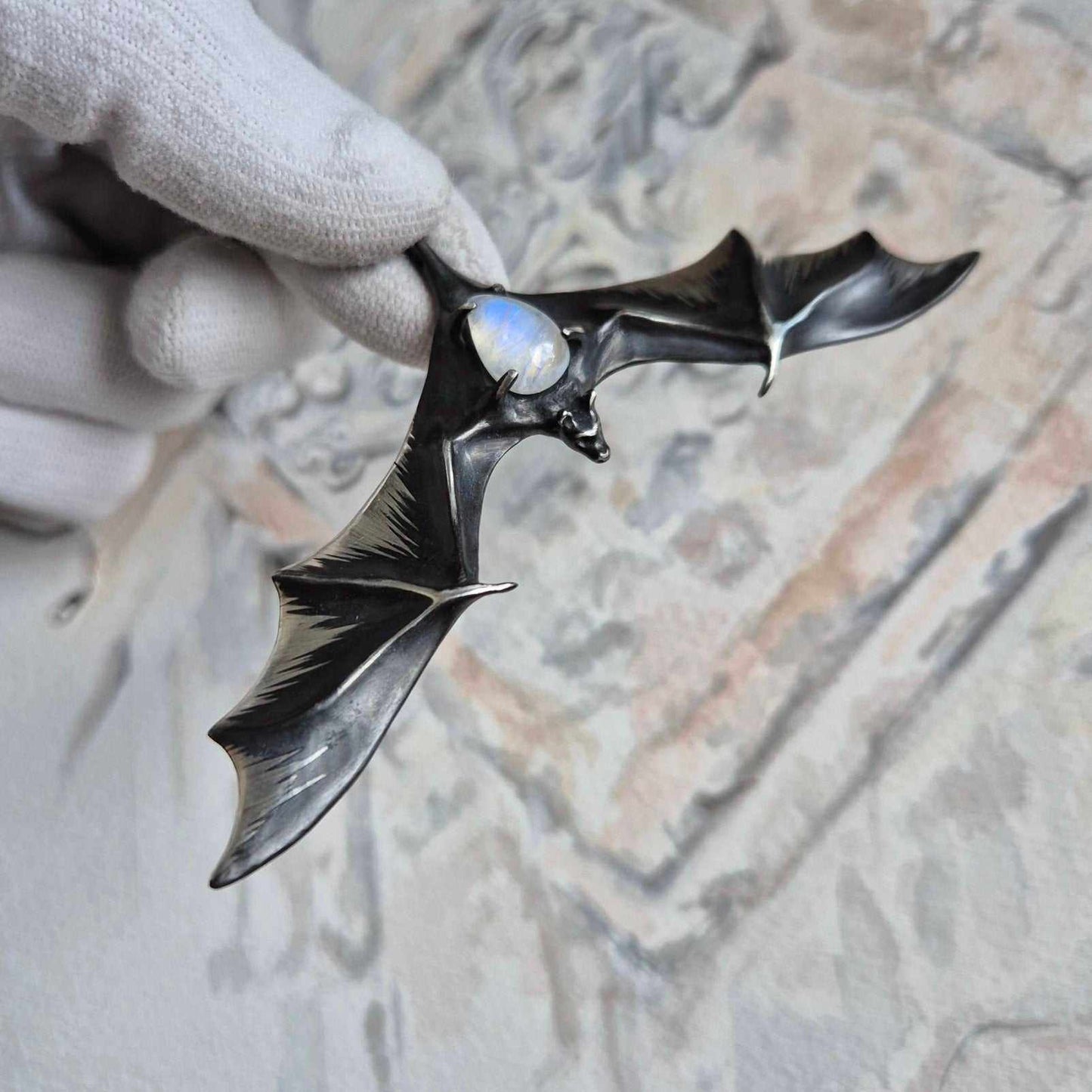 Silver Bat pendant with moonstone gemstone, shown in hand to highlight size and shine.