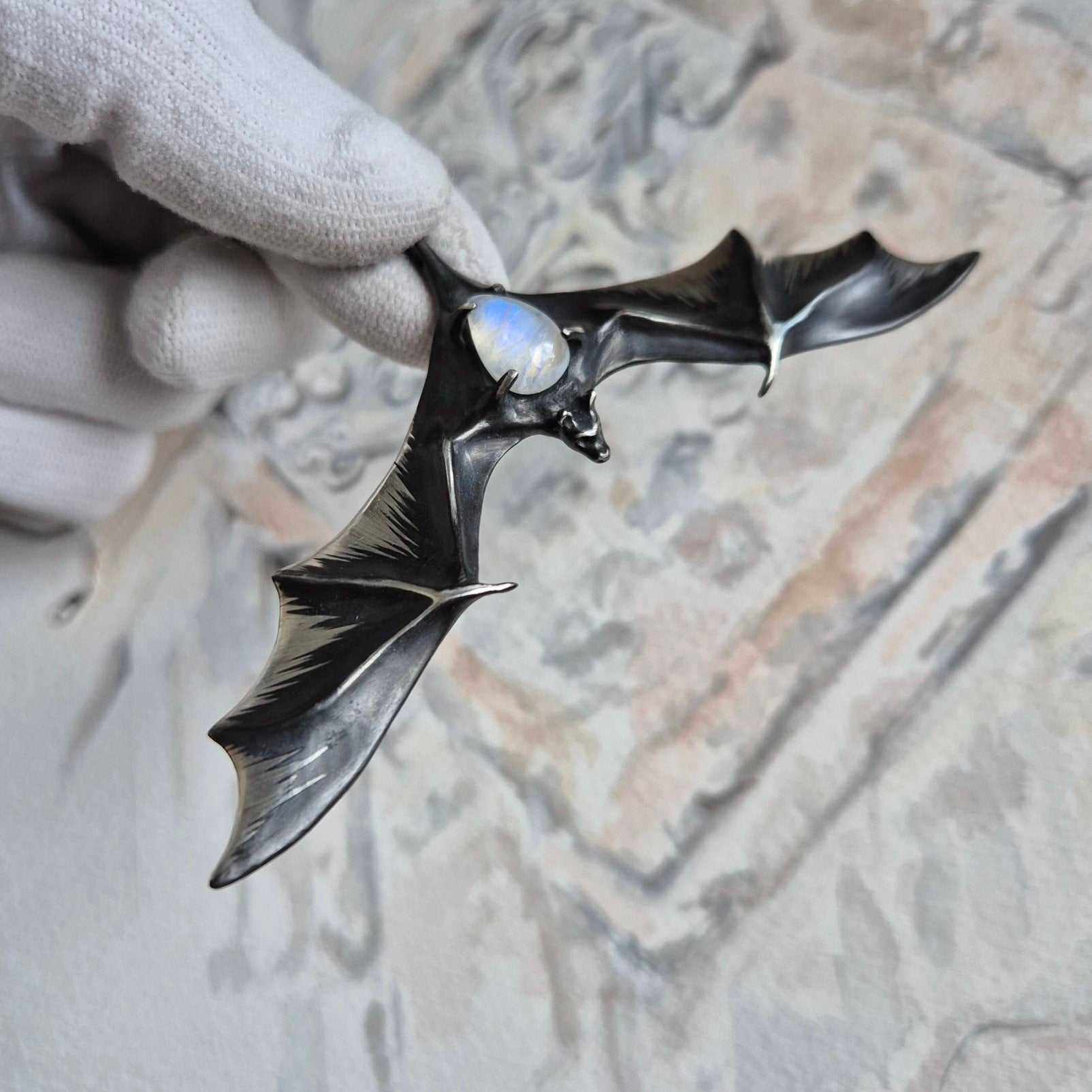 Silver Bat pendant with moonstone gemstone, shown in hand to highlight size and shine.