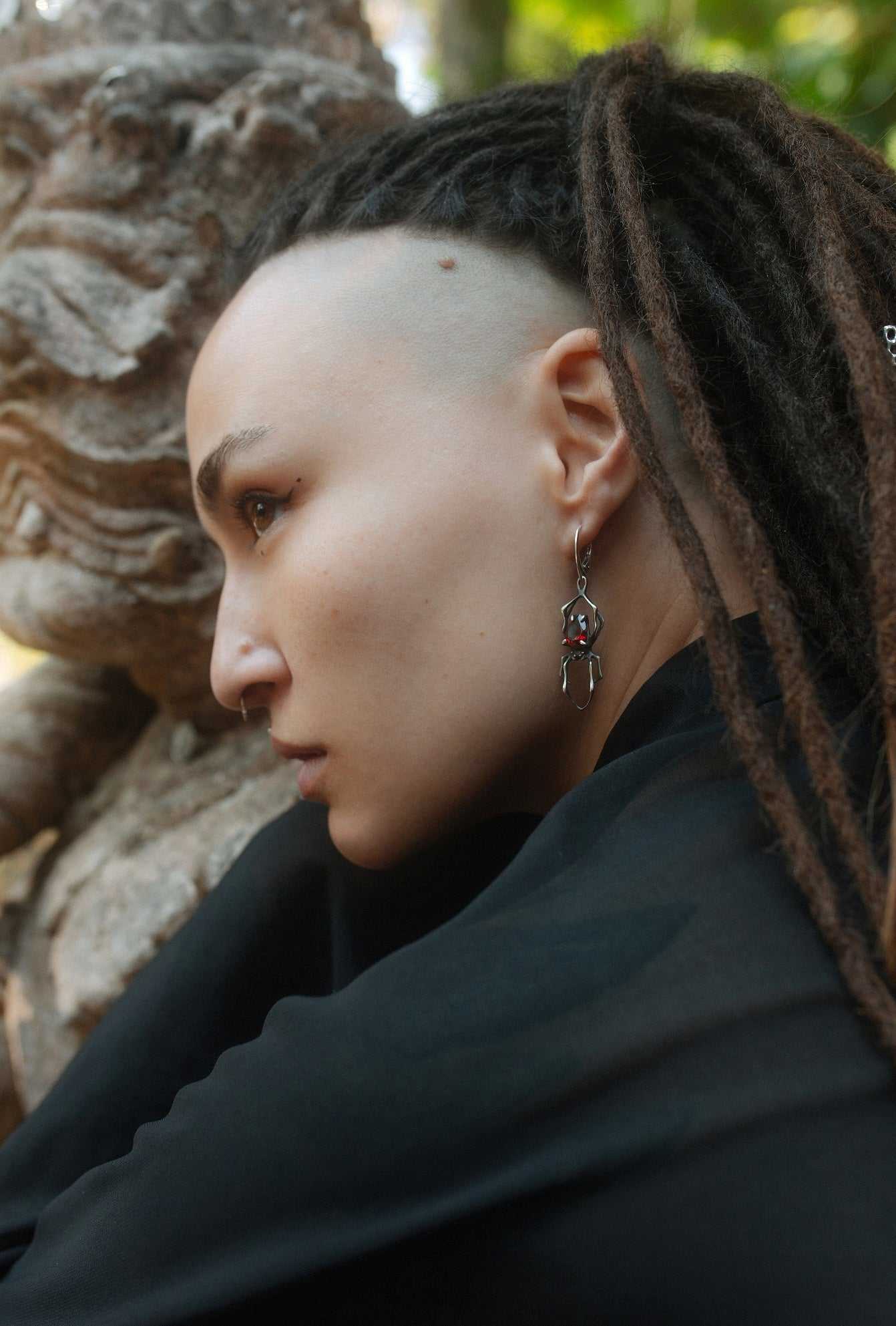 Close-up of handmade oxidised silver spider earrings with natural garnets, worn by a model with dreadlocks with shamanic vibe