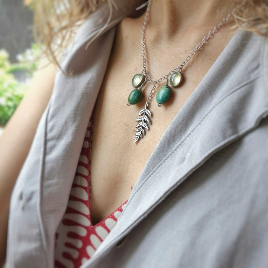 Handmade forest-inspired turquoise necklace with turquoise, prehnite, and a silver leaf charm, shown on a woman in natural light and layered clothing.