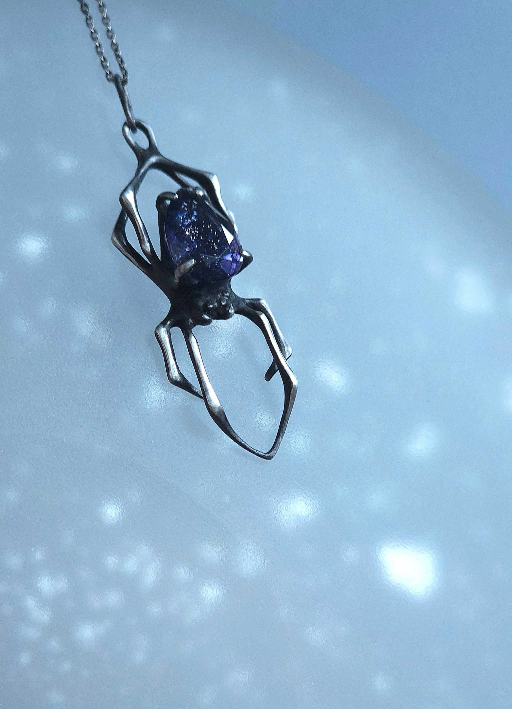Sterling silver spider pendant with speckled blue gemstone in soft lighting