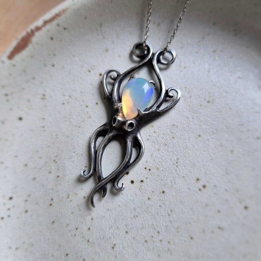 Handmade silver Octopus pendant featuring colorful opal, shown against a neutral ceramic plate.