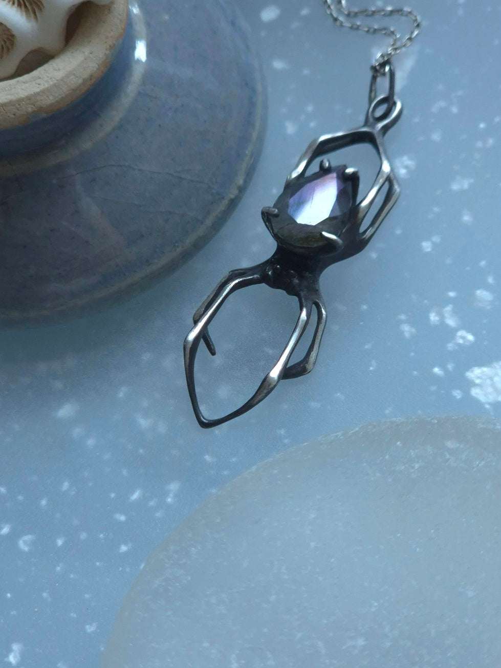 Side view of silver Spider pendant with luminous purple labradorite, resting on textured blue surface