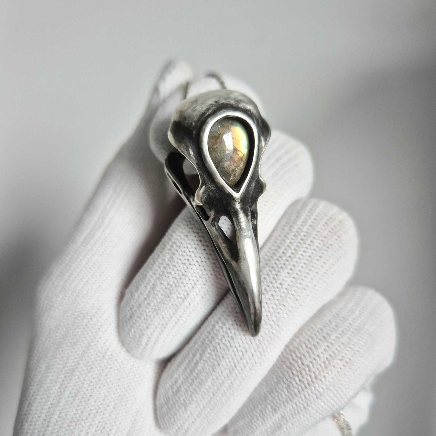 Close-up of handcrafted silver raven skull pendant with labradorite, on hand