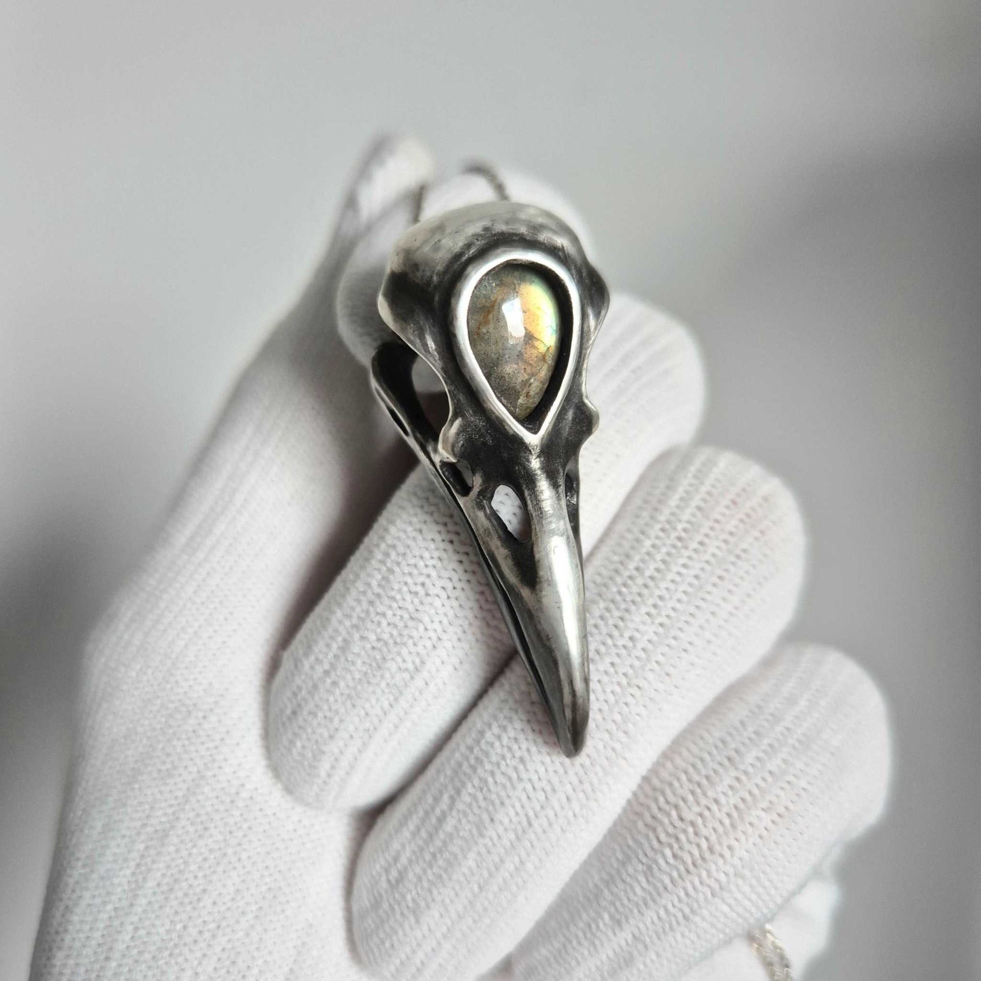 Close-up of handcrafted silver raven skull pendant with labradorite, on hand