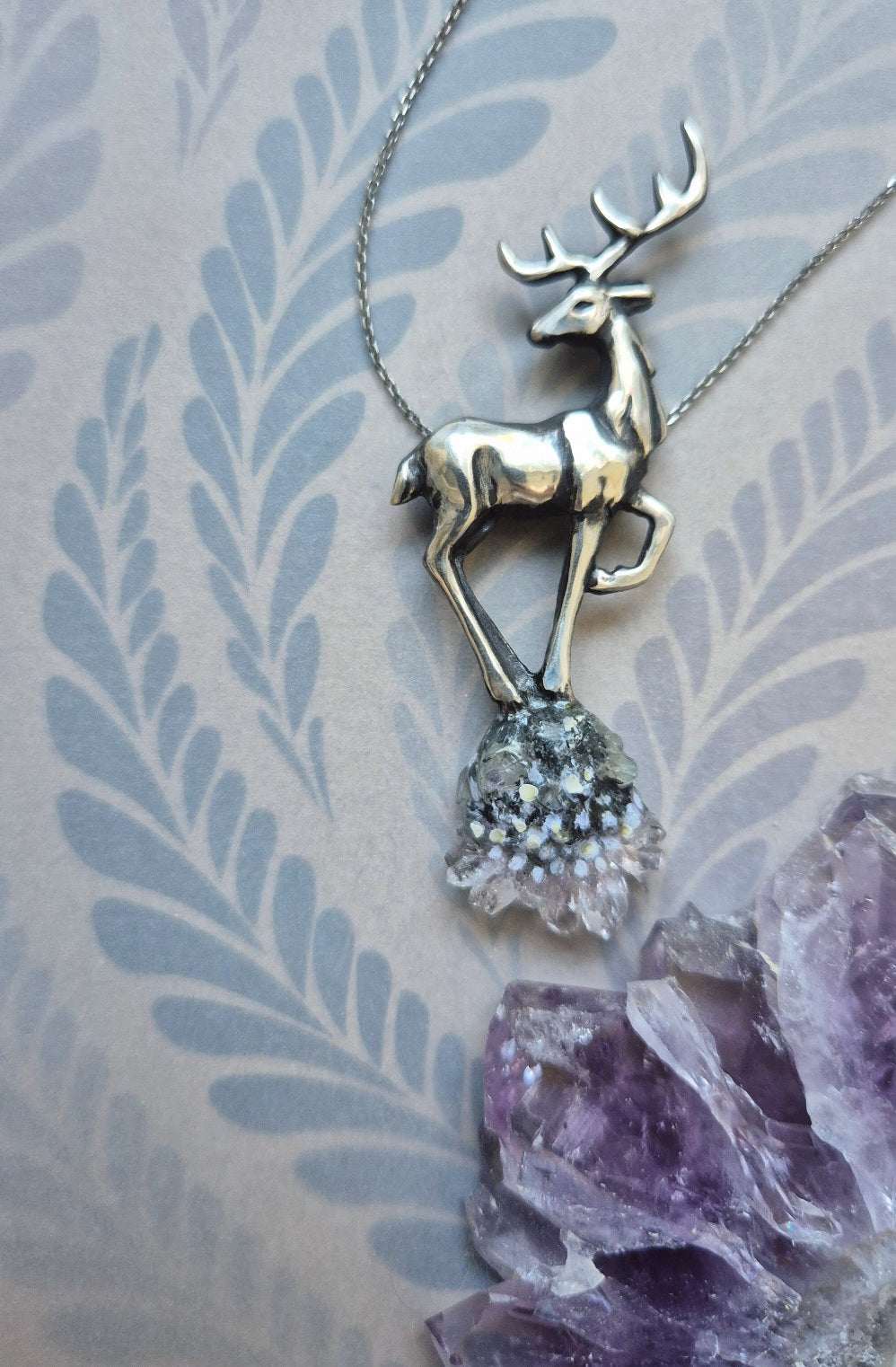 Silver deer necklace with raw crystal drop, resting on pastel botanical background with gentle light