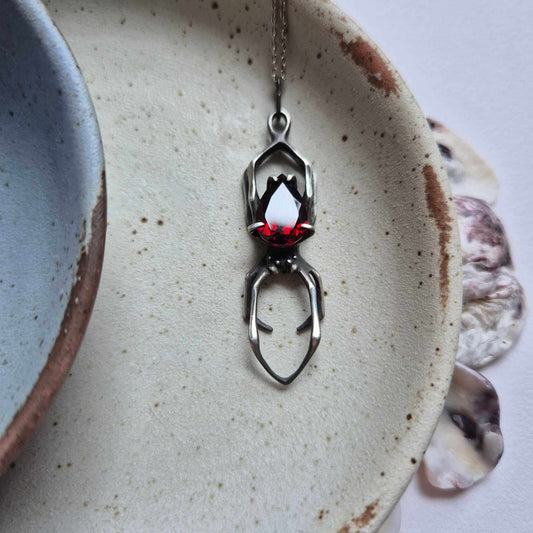 Silver Spider necklace with garnet gemstone on white background – handmade oxidized silver jewelry