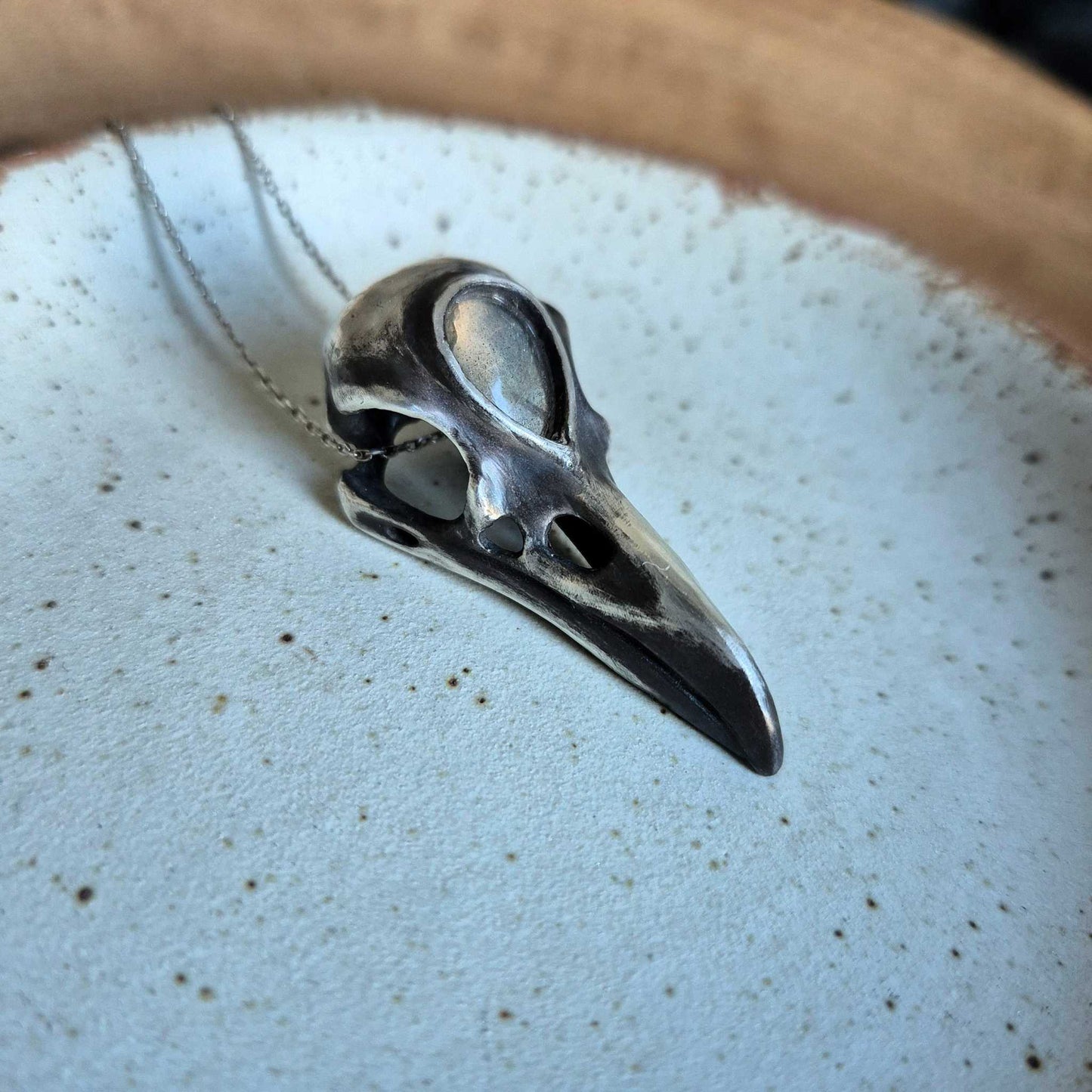 Handmade silver skull necklace with golden labradorite set in forehead, styled on ceramic plate.