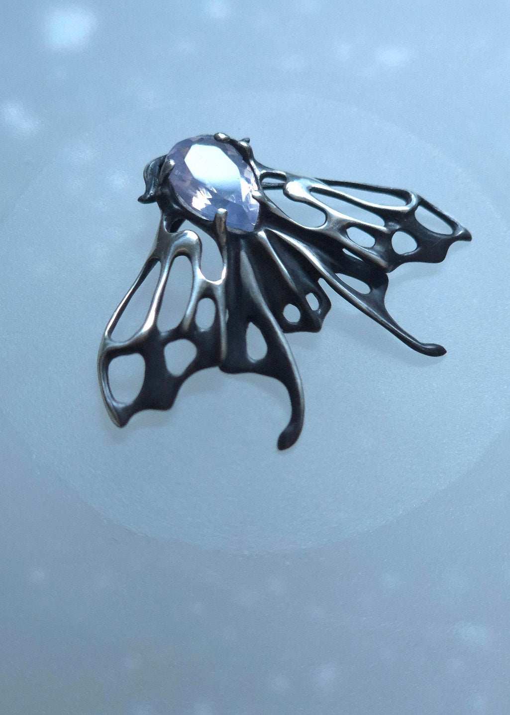 Close-up of handmade silver Moth necklace with shiny lavender quartz on soft background
