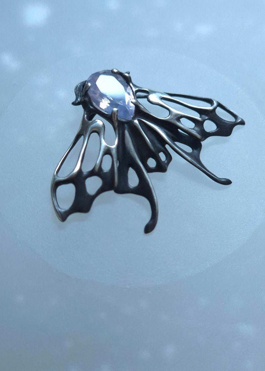 Close-up of handmade silver Moth necklace with shiny lavender quartz on soft background