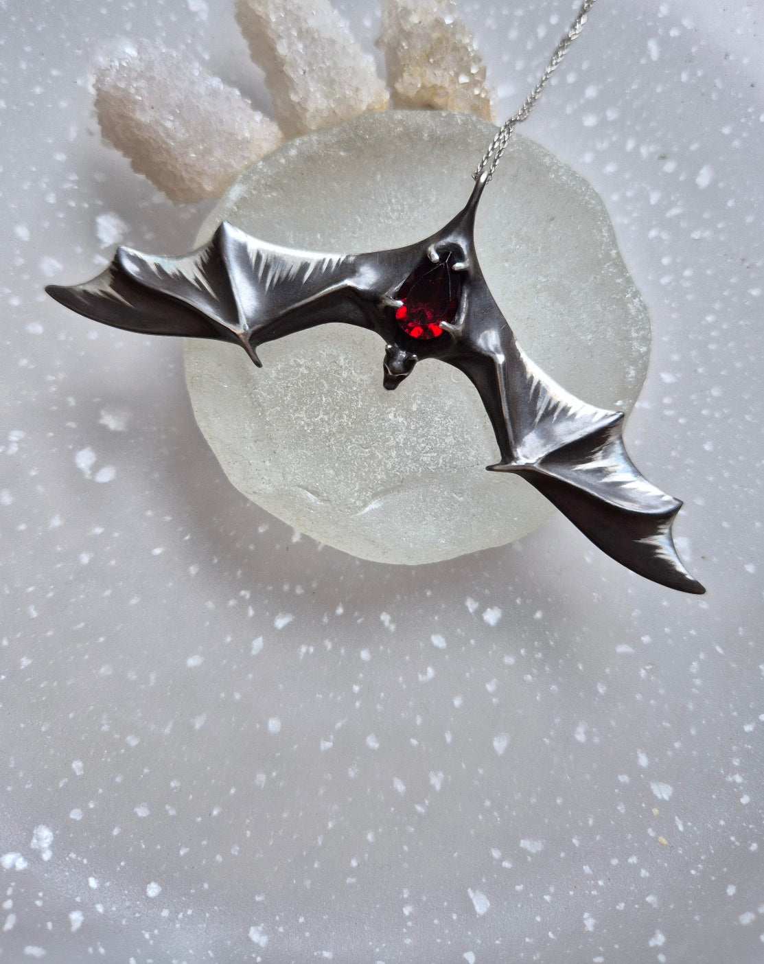 Front view of the Silver Bat necklace with deep red natural garnet glowing under light.