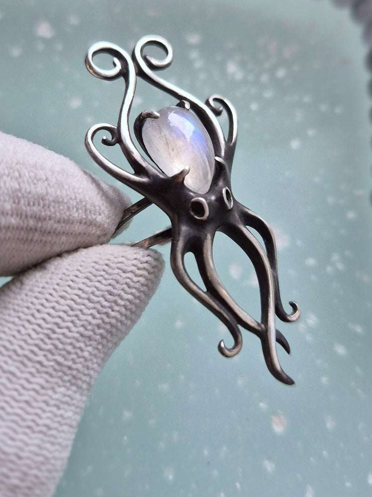 Octopus ring with moonstone beside agate beads necklace over pale aqua surface