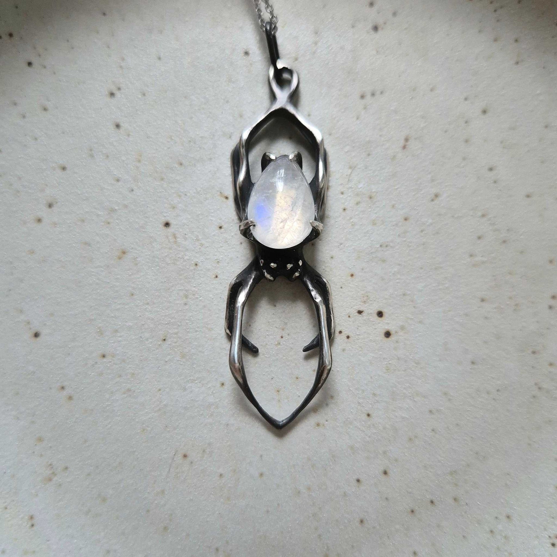 Close-up of a rainbow moonstone silver Spider necklace on ceramic background