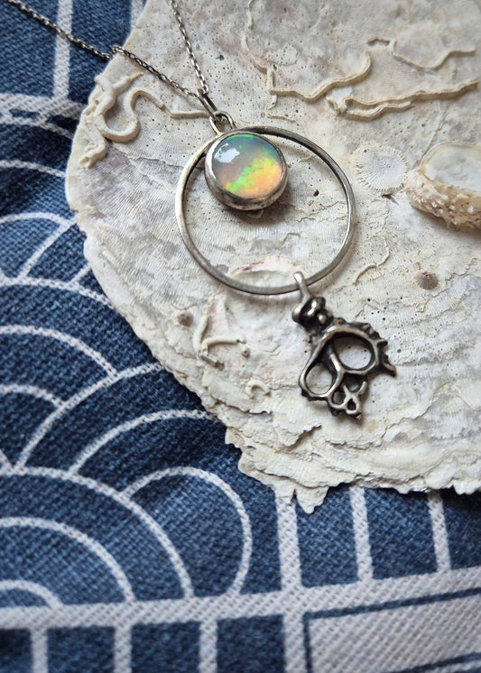 Ethereal opal pendant necklace with silver shell drop — handmade ocean-inspired jewelry displayed on a seashell on blue fabric