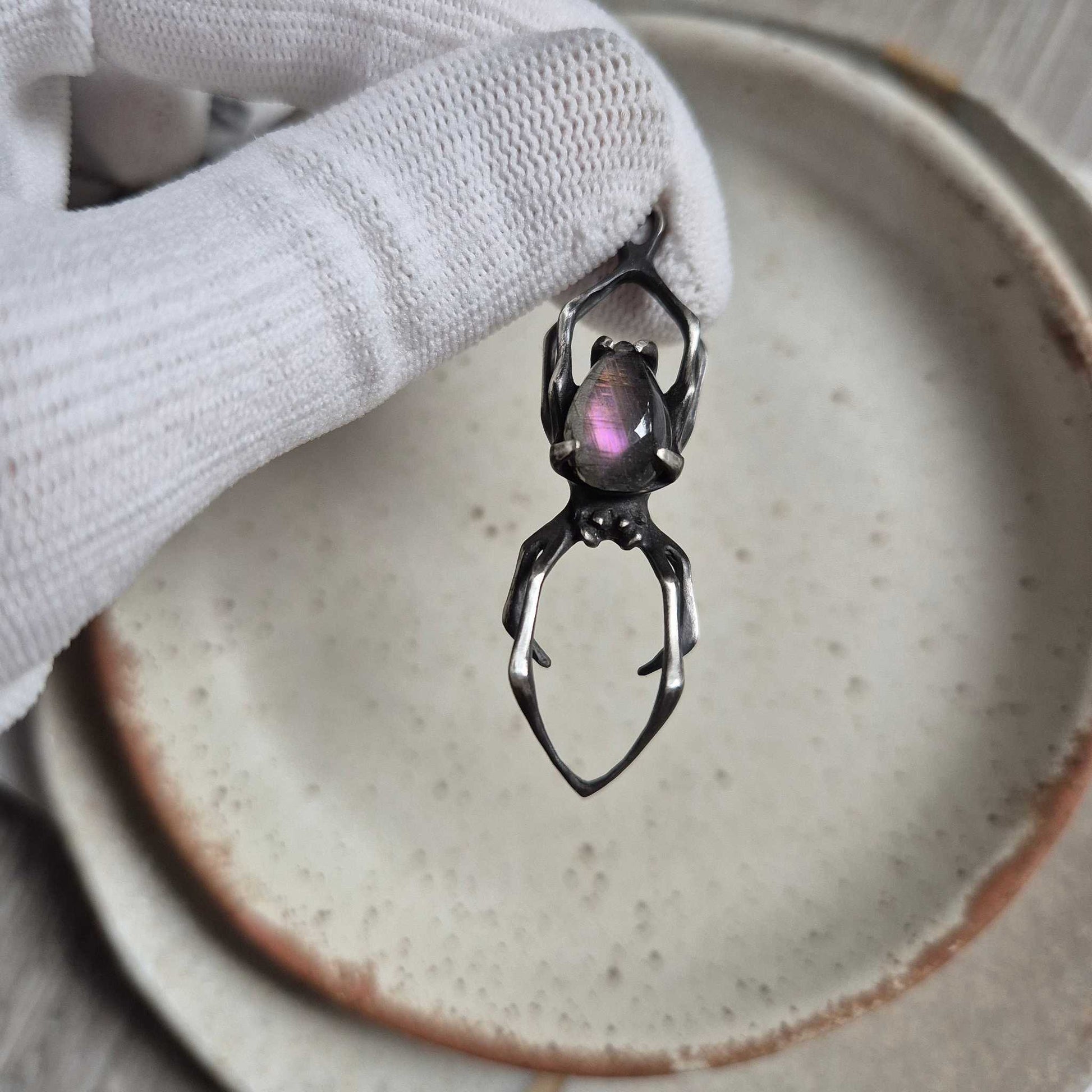Artisan silver Spider necklace featuring purple labradorite gem, viewed from side angleDetailed shot of Spider necklace with purple labradorite held in gloved hand